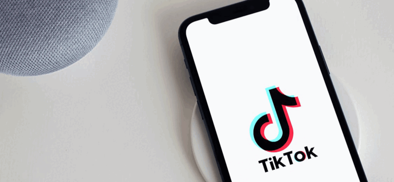iPhone loading in the TikTok app wirelessly charging next to a Google Alexa on a white desk